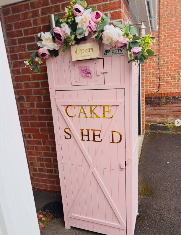 The pink Cake Shed with flowers and an Open sign